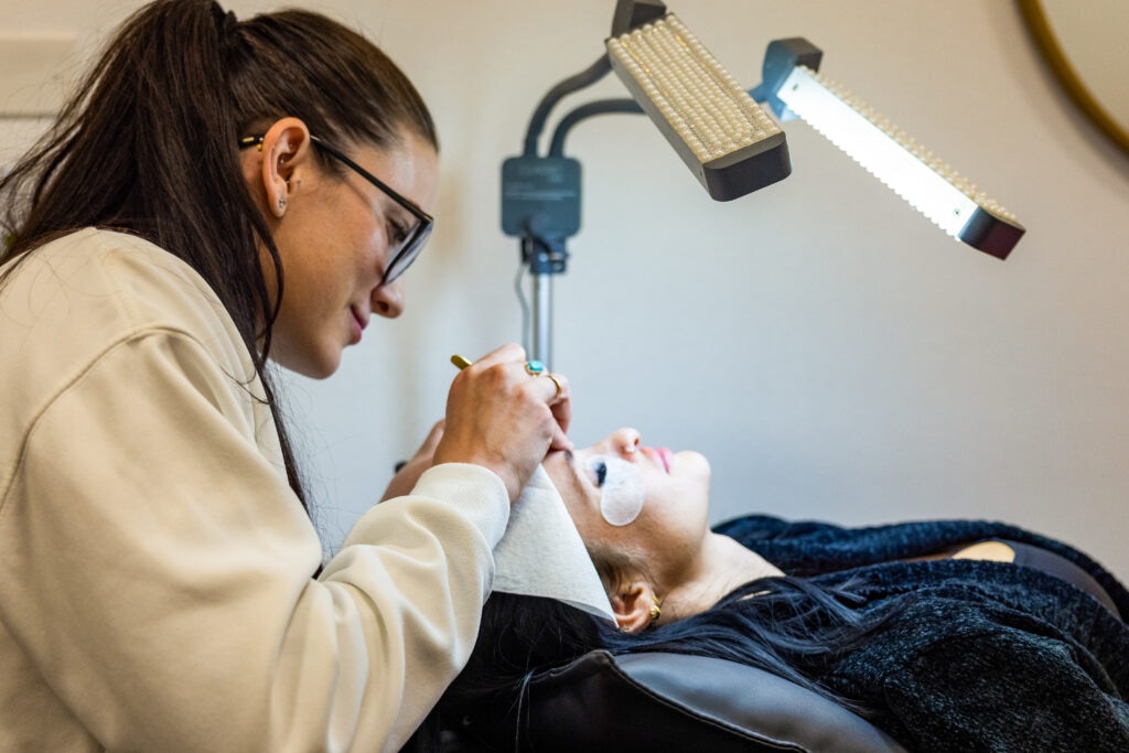 Esthetician applying eyelash extensions to client.