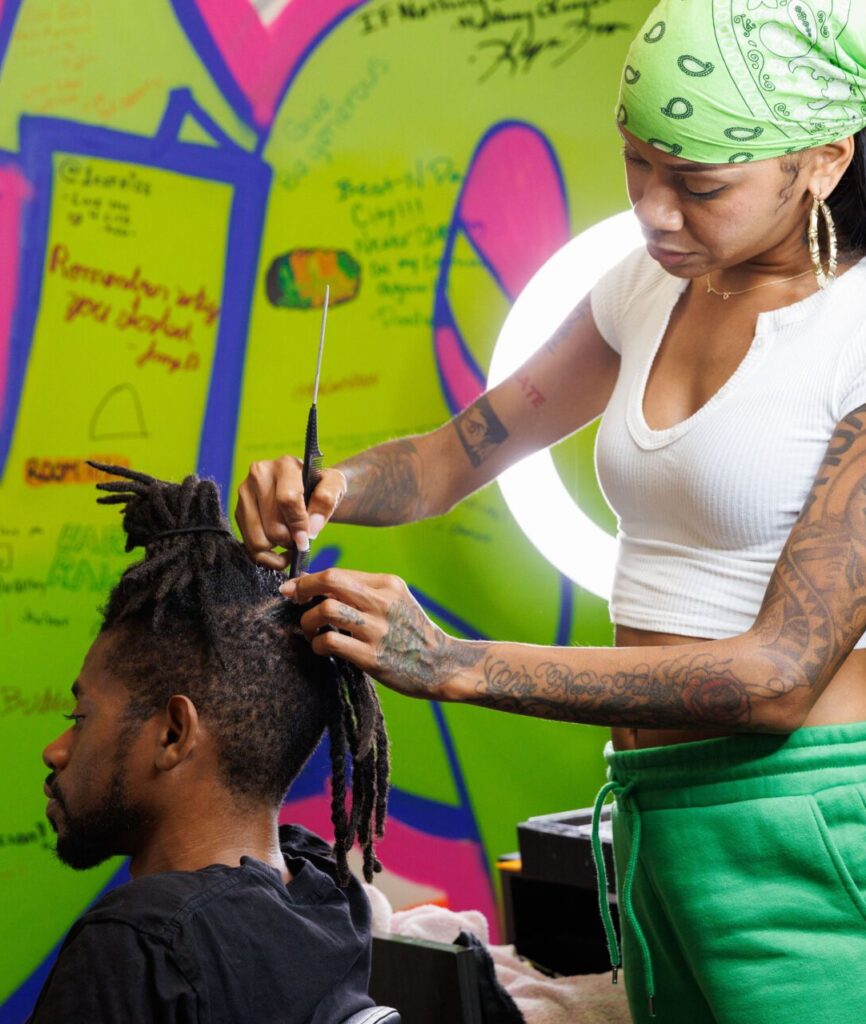 Stylist braiding hair in colorful salon.