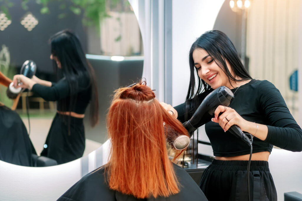 Stylist blow-drying client's hair in salon.
