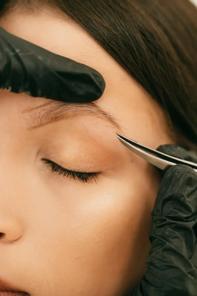 Close-up eyebrow tweezing with black gloves.