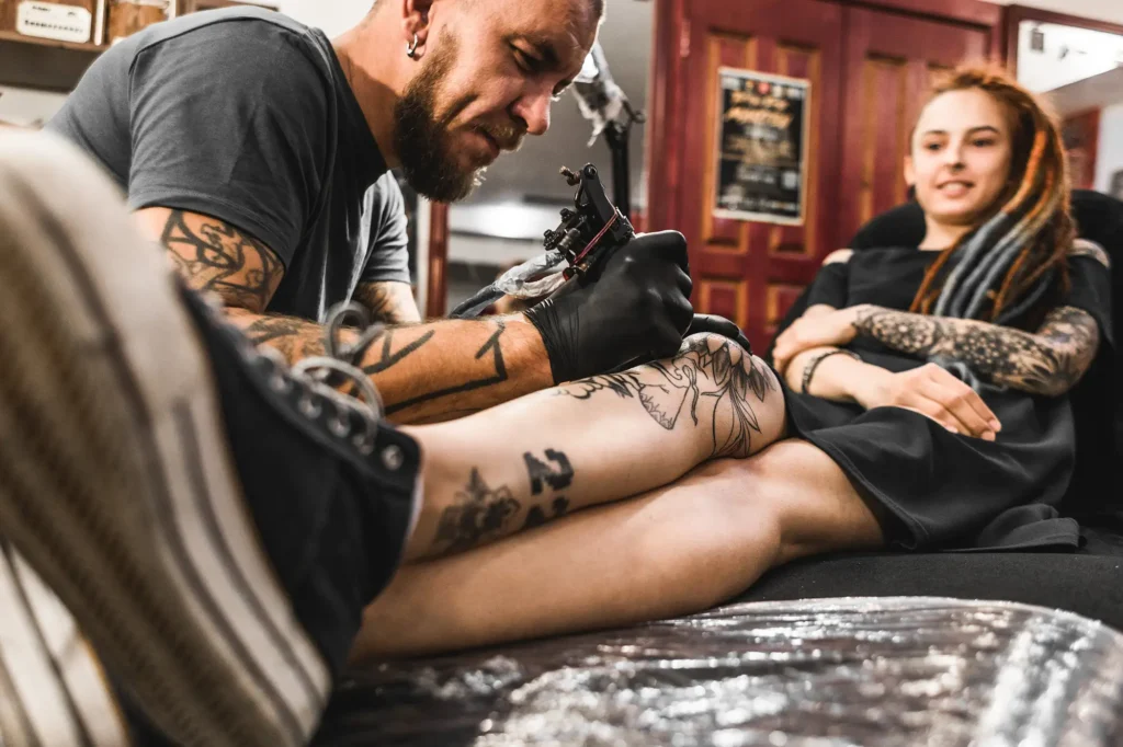 Tattoo artist working on client's leg tattoo.