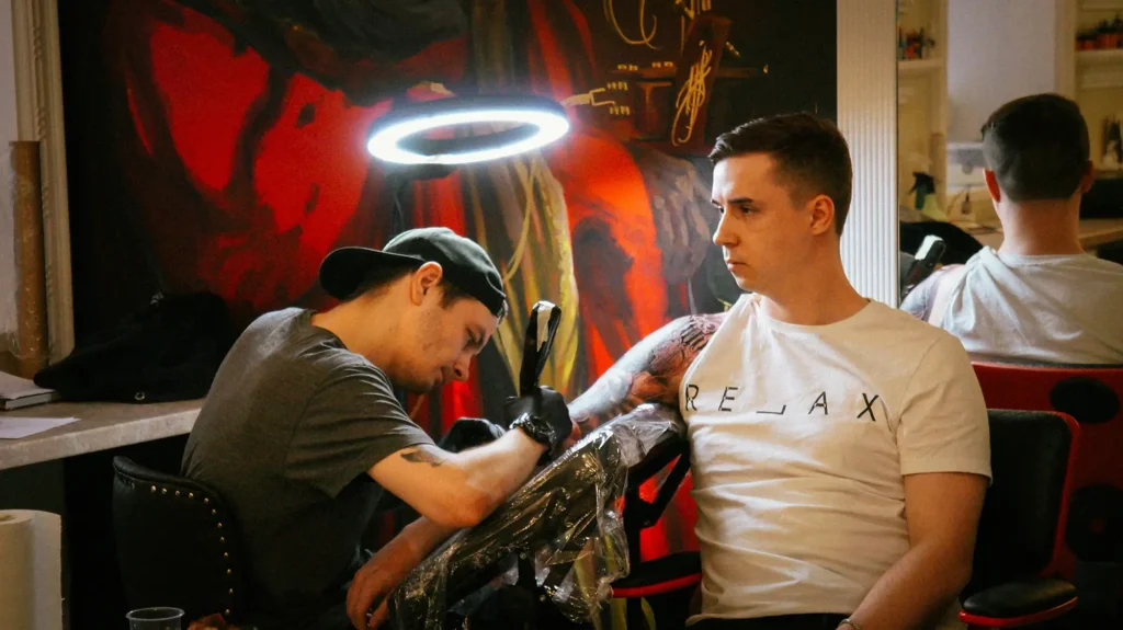 Tattoo artist working on client's arm under halo light.